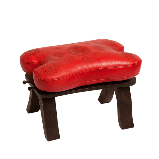 Moroccan stool with red embossed leather cushion and dark carved wooden legs, handcrafted in Morocco by skilled artisans.
