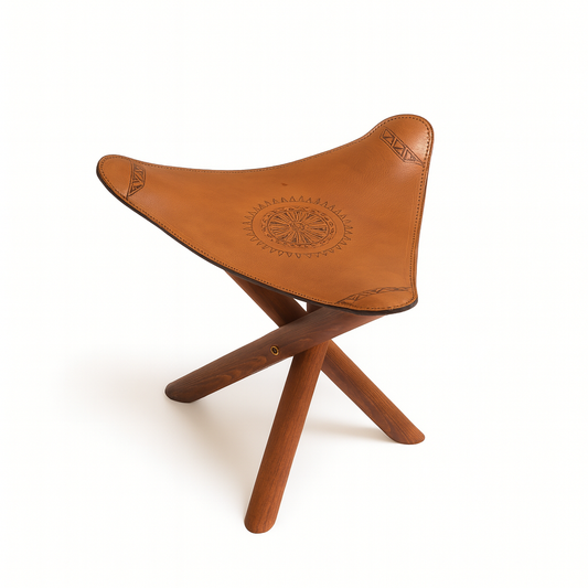 Handcrafted Moroccan stool with ocher leather seat and dark wooden tripod legs inspired by nomadic craftsmanship.
